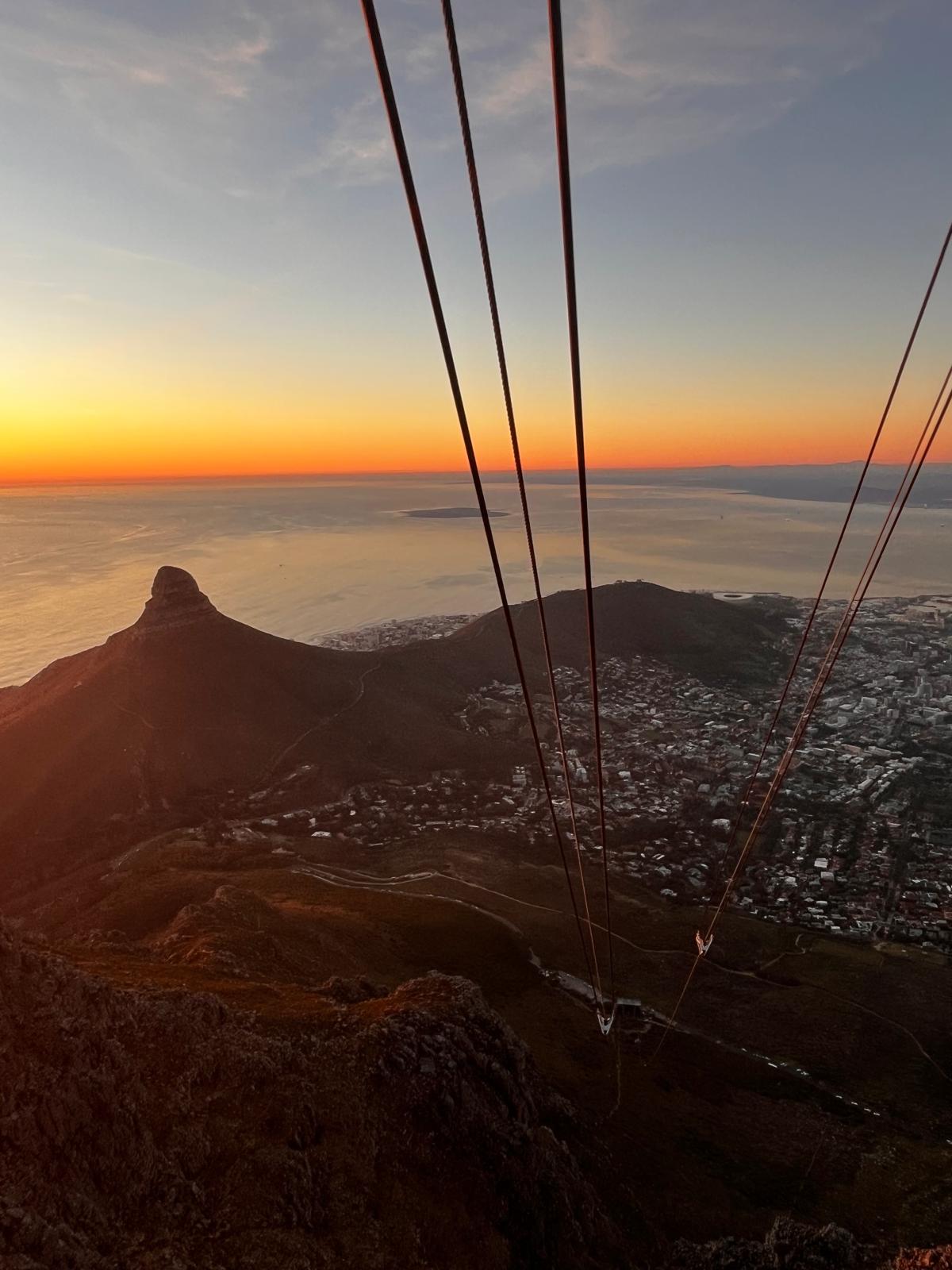 Tafelberg-Aussicht bei Abendlicht. Panoramablick von der Bergstation Tafelberg auf Kapstadt bei Dämmerung, Tragseile der Seilbahn im Vordergrund.