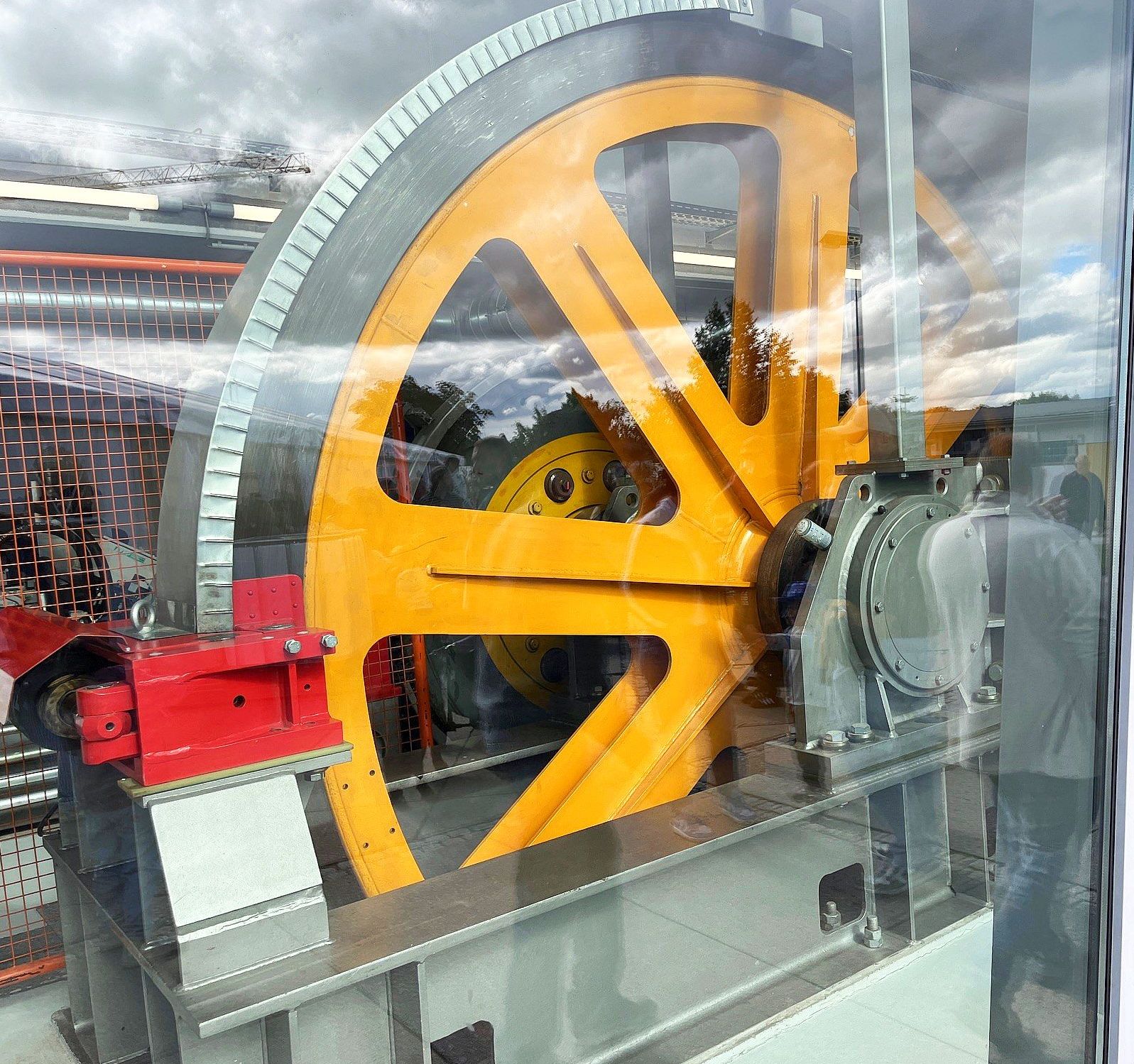 Orangefarbenes Antriebsrad der Bergbahn hinter einer Glasscheibe sichtbar
