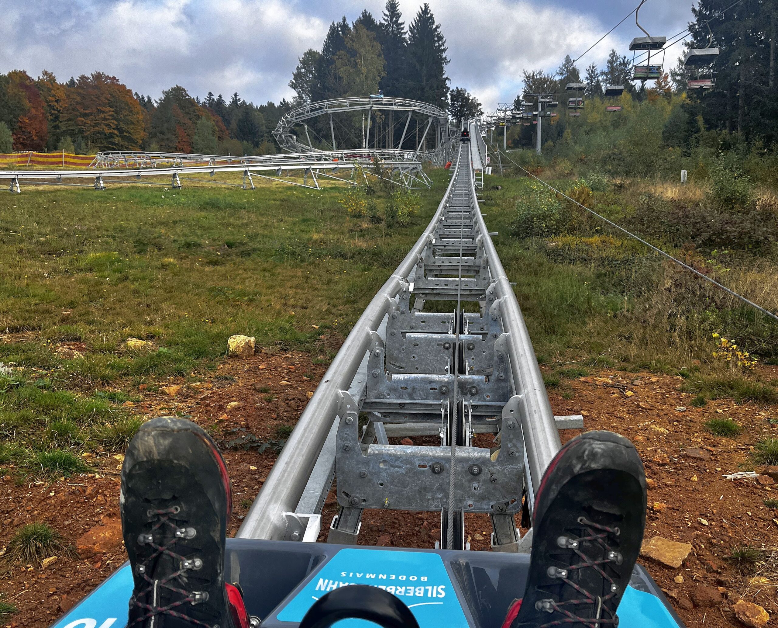 Blick auf Füße im Schlitten des Alpin Coasters auf Metall-Schienen während Testfahrt