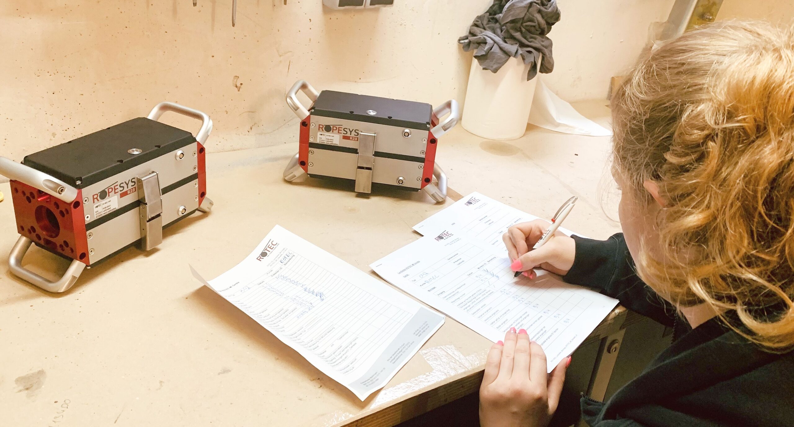 ROTEC-Mitarbeiterin Tamara bei Aufzeichnungen in der Werkstatt, Blick von hinten auf die Seilprüfgeräte