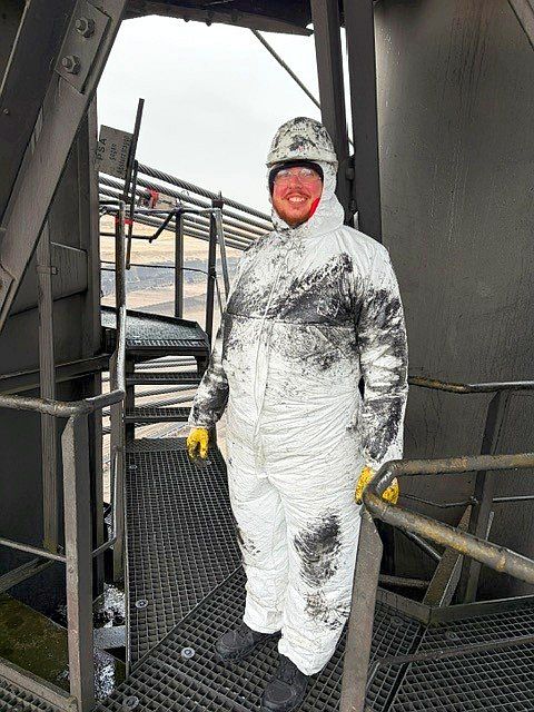 Ein Techniker im sehr verschmutzten, weiß-schwarzen Schutzanzug auf Metallgitter.