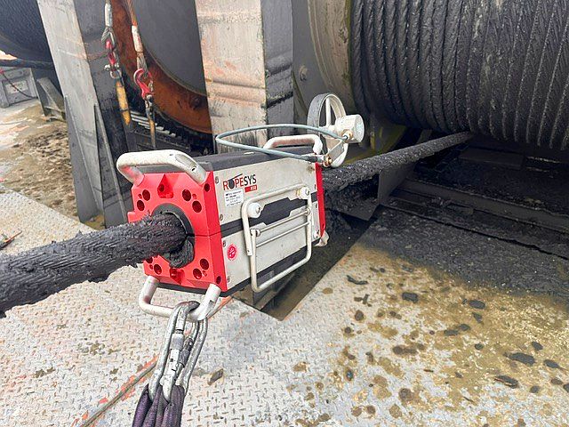 Das ROPESYS Seilprüfgerät an einem extrem fettverkrusteten Stahlseil direkt vor einer Seiltrommel.