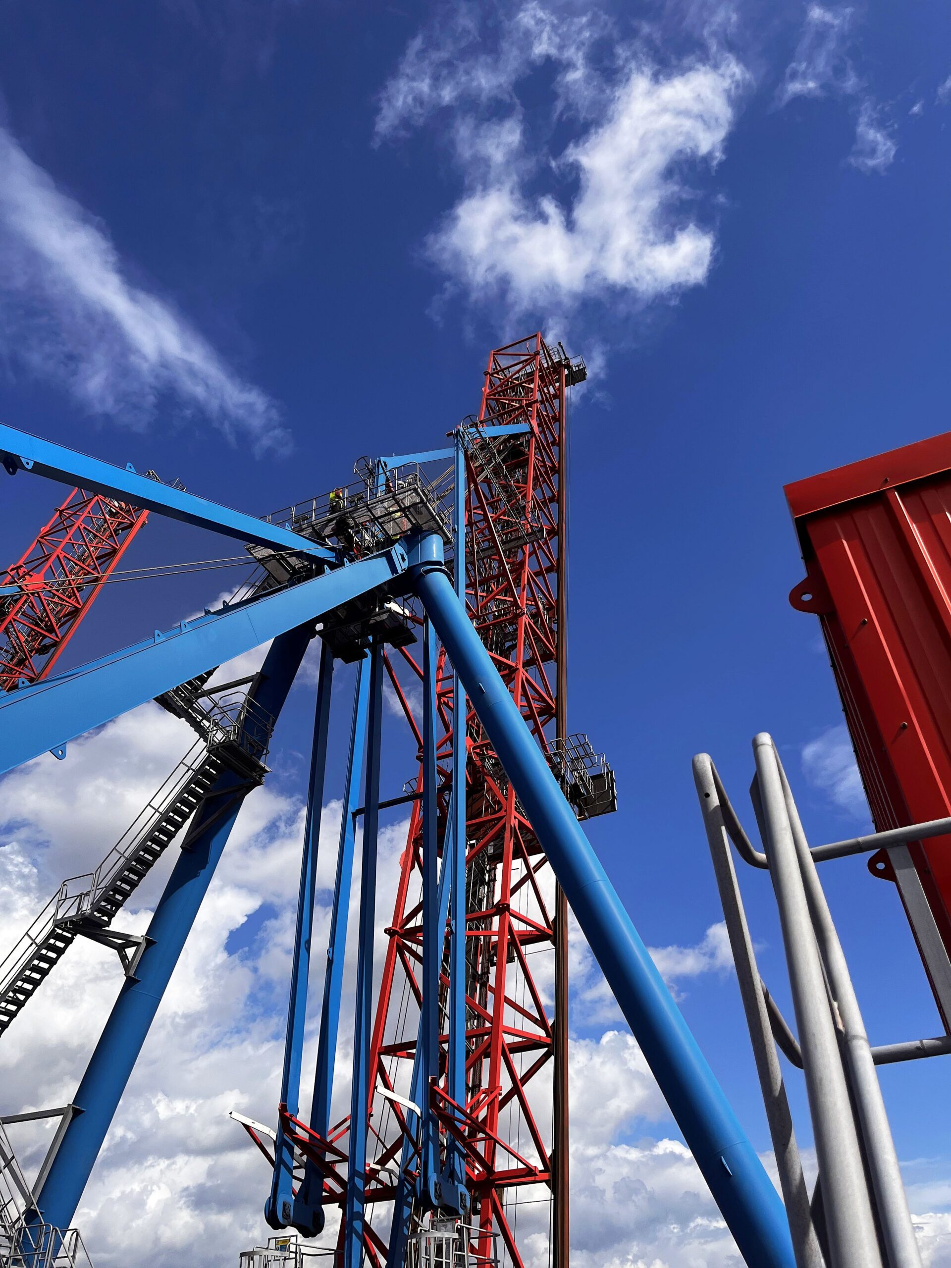 Stahlkonstruktion eines Containerkrans mit blauen Trägern, roten Gittermasten und Seilen.